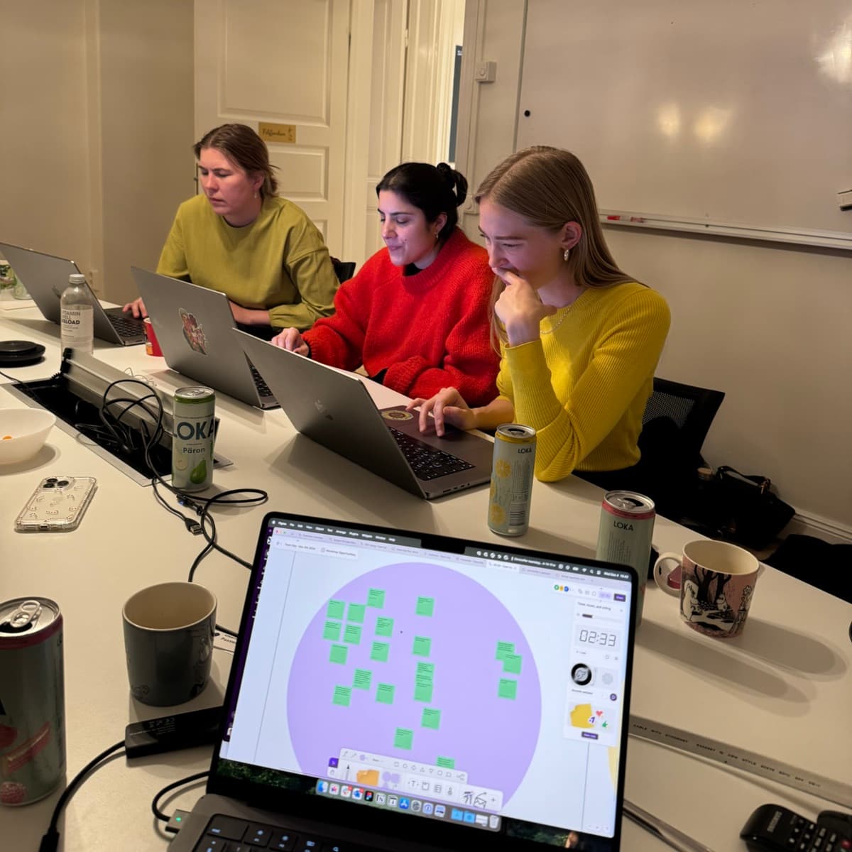 Three designers working side by side on laptops around a meeting table