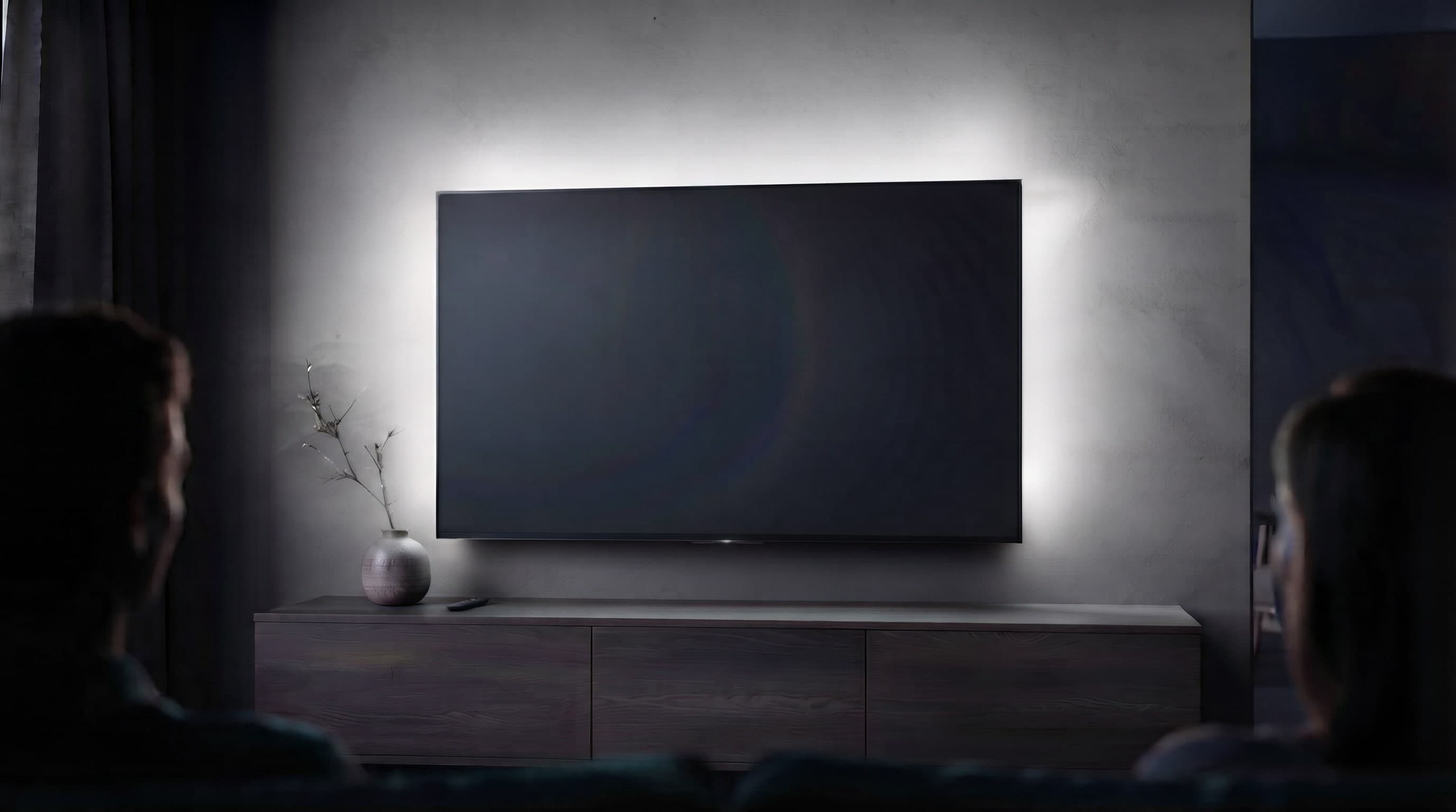 A dark living room with a wall-mounted TV, softly backlit