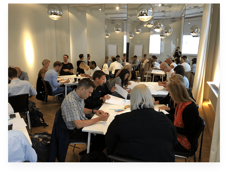 A room full of people from across Viaplay sketching ideas at long tables during the design studio